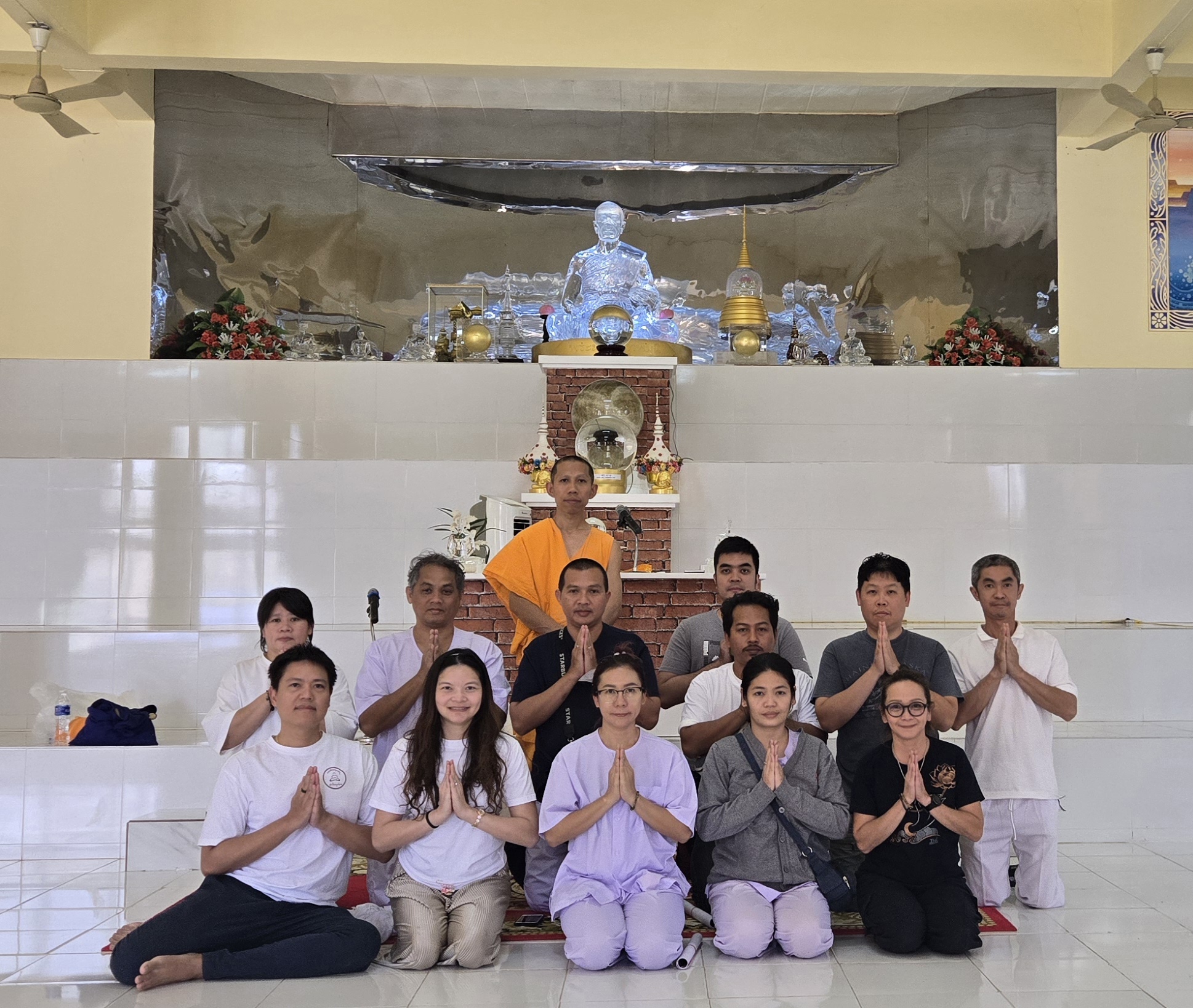 หมู่คณะพนมมือถ่ายภาพร่วมกับพระสงฆ์เบื้องหน้าพระพุทธรูปแก้วใส